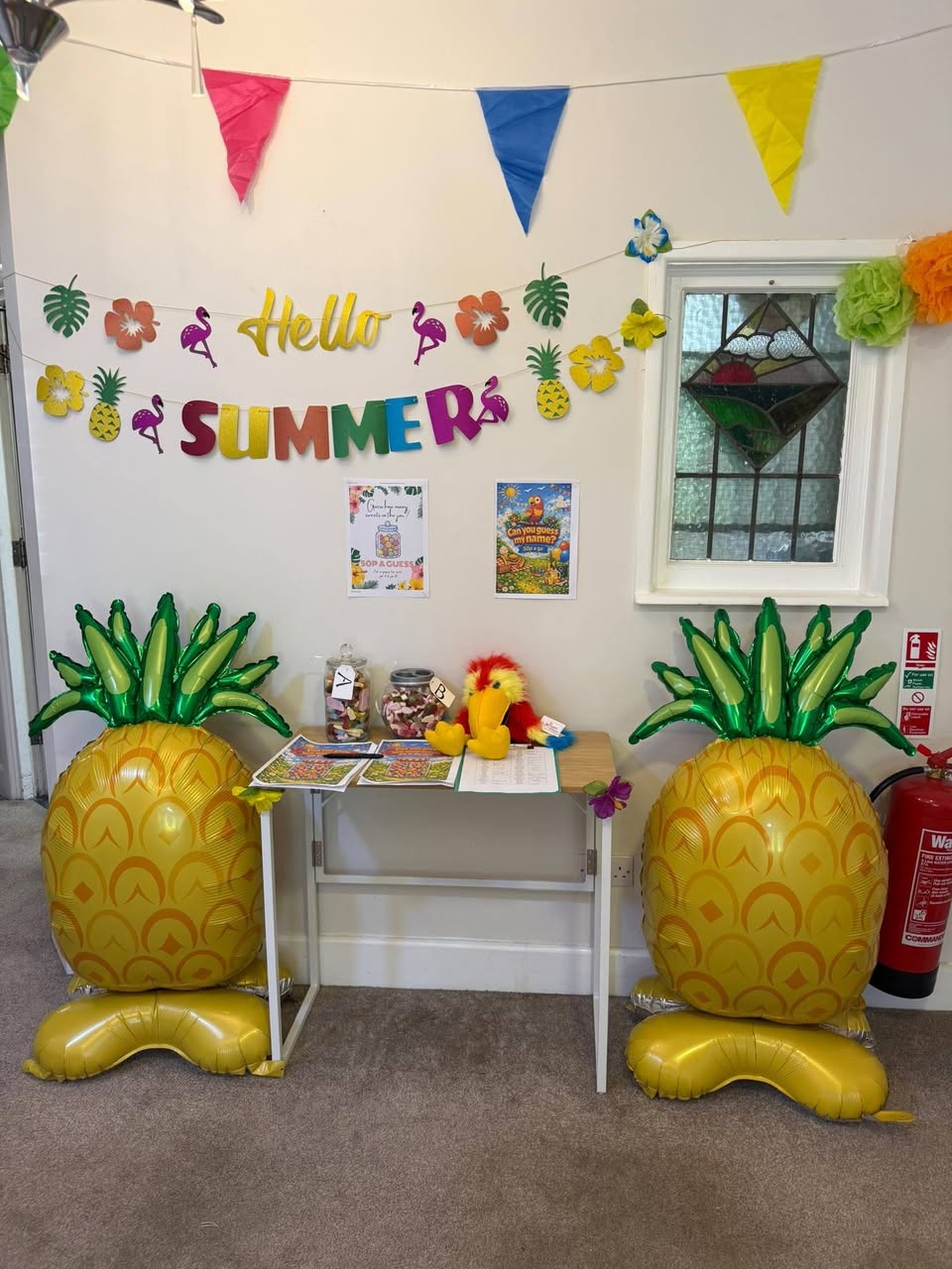 Indoor Summer Party display with colourful bunting, a Hello Summer sign, tropical decorations and two large pineapple balloons.