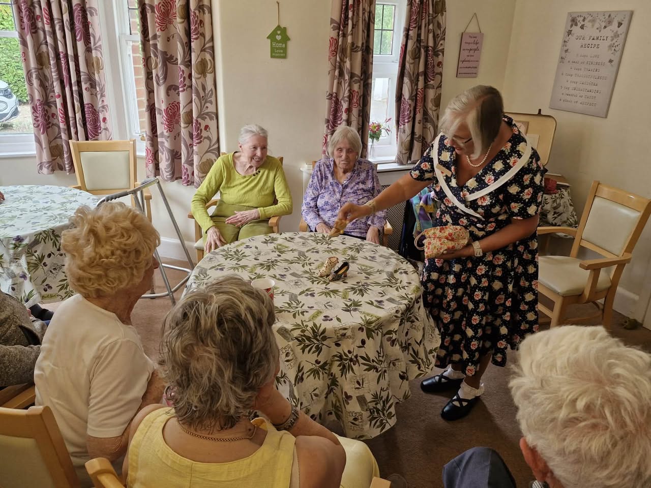 Memory-session group seated around a table while a participant in a vintage-style floral dress presents an activity.